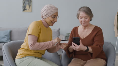 Arabic-Woman-Teaching-An-Elderly-Woman-To-Use-Mobile-Payment-With-Credit-Card-2