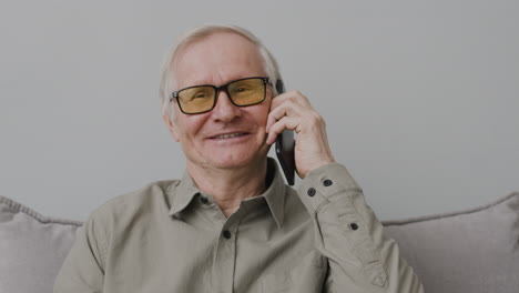Anciano-Feliz-Llamando-Por-Teléfono-Mientras-Está-Sentado-En-La-Sala-De-Estar-En-Casa