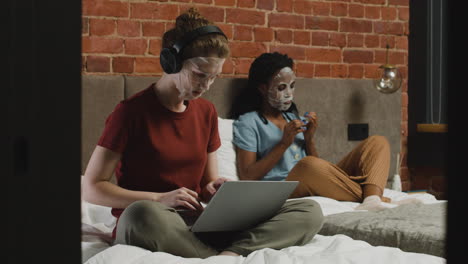 And-Girls-With-Facial-Mask-Listening-To-Music-On-Laptop-And-Filing-Her-Nails-In-Bed