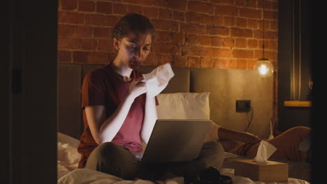 Girl-Watching-Videos-On-Laptop-While-Cleanig-Her-Face-With-A-Paper-Towel-In-Bedroom-At-Night