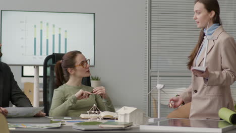 Woman-Explaining-Wind-Turbine-Model-And-Discussing-About-Renewable-Energy-Project-With-Her-Colleagues-In-The-Office-1