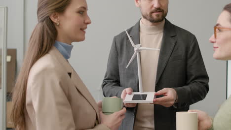 Businessman-Explaining-Wind-Turbine-Model-To-Two-Women-In-The-Office