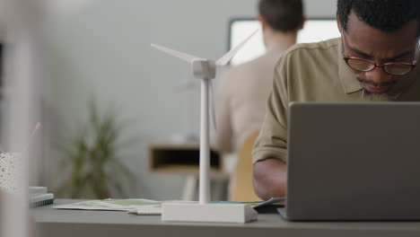Businessman-Using-Laptop-Sitting-At-Table-With-Windmill-Model-In-The-Office-1