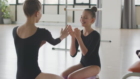 Two-Gymnastic-Blonde-Girls-Playing-To-Hand-Clapping-Game-Sitting-On-The-Floor-Before-Starting-Ballet-Class-1