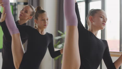 Dos-Chicas-Rubias-Gimnásticas-Ensayando-Un-Movimiento-De-Ballet-Frente-A-La-Barra-De-Ballet