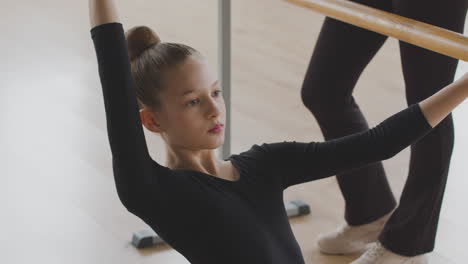 Gymnastic-Blonde-Girl-Rehearsing-A-Ballet-Move-In-Front-Of-Ballet-Barre-Sitting-On-The-Floor
