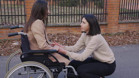 Woman-Squatting-Talking-With-Her-Female-Disable-Friend-In-Wheelchair-In-The-Street