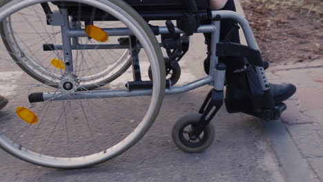 Die-Kamera-Fokussiert-Auf-Räder-Eines-Rollstuhls,-Die-Sich-Auf-Einem-Spaziergang-Auf-Der-Straße-Drehen-1