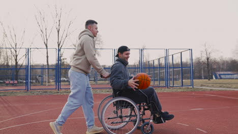 Young-Disabled-Man-Bouncing-The-Ball-And-Throwing-It-Into-The-Basketball-Hoop-While-His-Friend-Pushing-Him