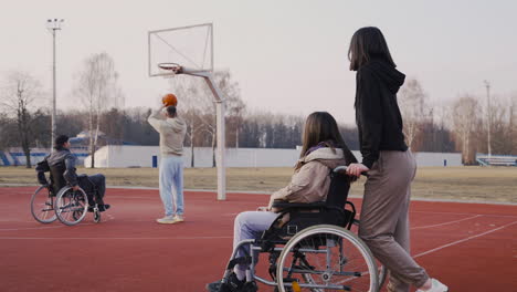 Mujer-Discapacitada-En-Silla-De-Ruedas-Y-Su-Amiga-Mirando-A-Sus-Amigos-Jugando-Al-Baloncesto
