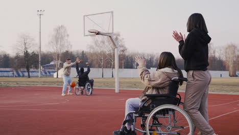 Behinderte-Frau-Im-Rollstuhl-Und-Ihre-Freundin,-Die-Ihren-Freunden-Zusieht,-Wie-Sie-Basketball-Spielen-2