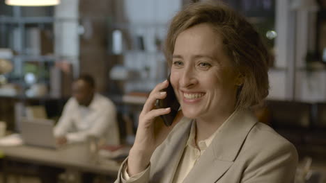 Portrait-Of-A-Smiling-Businesswoman-Talking-On-Mobile-Phone-While-Standing-In-The-Office