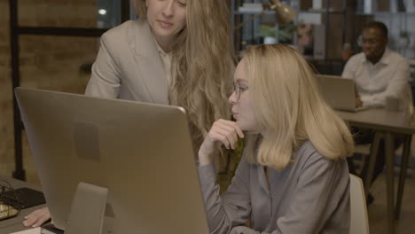 Two-Female-Employees-Looking-Something-At-Computer-And-Talking-Together-In-The-Office-2