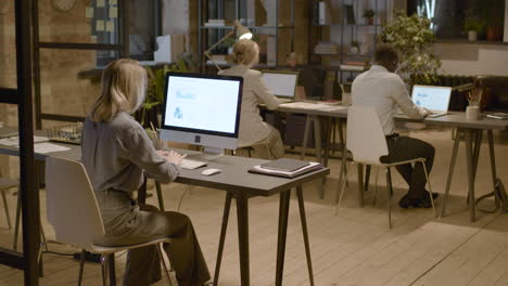Rear-View-Of-Three-Coworkers-Sitting-At-Desk-While-Watching-Stadistics-And-Graphics-On-Computer-Monitor