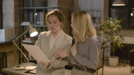 Two-Female-Coworkers-Talking-And-Reading-A-Document-Standing-In-The-Office