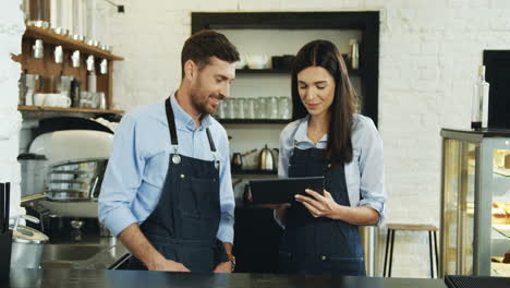 Waitress-And-Waiter-Smiling-And-Watching-Something-On-The-Tablet-While-Standing-At-The-Bar-In-The-Cafe