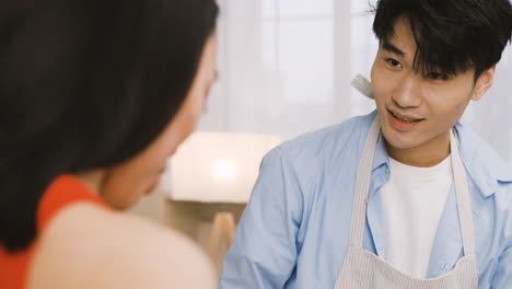 Close-Up-View-Of-A-Japanese-Man-Wearing-An-Apron-While-Cooking-And-Talking-With-A-Friend-In-The-Kitchen