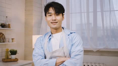 Close-Up-View-Of-Japanese-Man-Wearing-Apron-Looking-And-Smiling-At-The-Camera-In-The-Kitchen