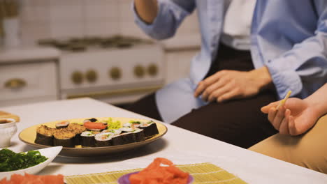 Japanischer-Mann,-Der-Ein-Stück-Sushi-Mit-Stäbchen-Auswählt-Und-Es-Seinem-Freund-Zum-Probieren-Gibt