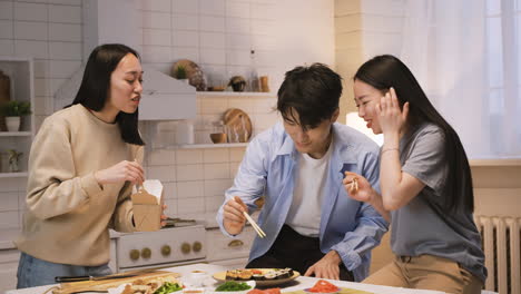 Three-Japanese-Friends-Eating-Ramen-And-Sushi-In-The-Kitchen