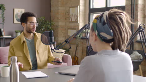 Young-Man-Sitting-At-A-Table-With-Microphones-And-Computer-To-Record-A-Podcast-With-A-Woman