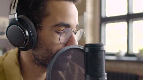 Close-Up-View-Of-Man-Recording-A-Podcast-Wearing-Eyeglasses-And-Headphones-And-Talking-Into-A-Microphone