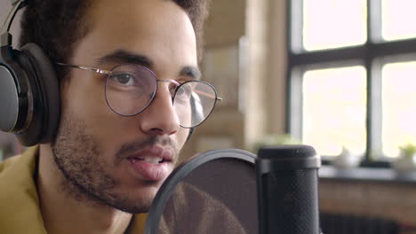 Close-Up-View-Of-Man-Recording-A-Podcast-Wearing-Eyeglasses-And-Headphones-And-Talking-Into-A-Microphone-1