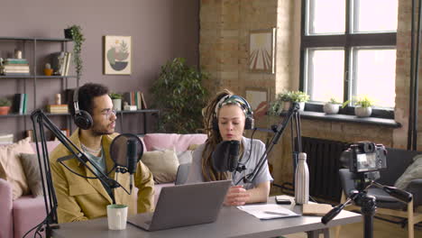 Cuc-Woman-And-Man-With-Headphones-Are-Sitting-At-Table-With-Microphone-And-Laptop-While-Recording-A-Podcast
