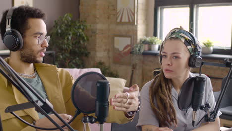 Young-Man-And-Woman-Wearing-Headphones-Sitting-At-A-Table-With-Microphones-While-They-Recording-A-Podcast