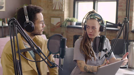 Young-Man-And-Woman-Wearing-Headphones-Sitting-At-A-Table-With-Microphones-While-They-Recording-A-Podcast-1