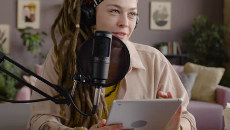 Close-Up-View-Of-Woman-With-Dreadlocks-Recording-A-Podcast-Talking-Into-A-Microphone-And-Holding-A-Tablet-Sitting-At-Desk