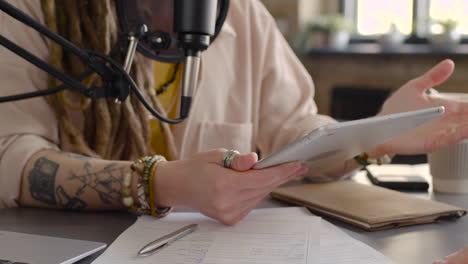 Close-Up-View-Of-Woman-Hands-Holding-And-Tapping-On-A-Tablet-While-Recording-A-Podcast-Talking-Into-A-Microphone