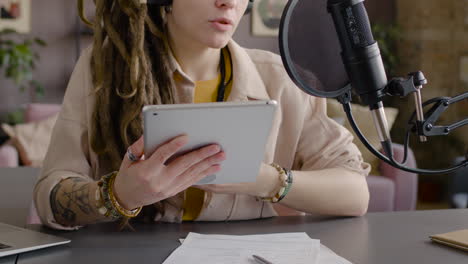 Close-Up-View-Of-Unrecognizable-Woman-With-Dreadlocks-Recording-A-Podcast-Talking-Into-A-Microphone-Sitting-At-Desk-With-Laptop-And-Documents