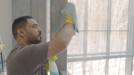 Close-Up-View-Of-Arabic-Cleaning-Man-Cleaning-The-Window-Panes-With-A-Rag-And-Glass-Cleaner-Inside-An-Office
