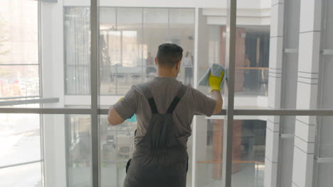 Rear-View-Of-Arabic-Cleaning-Man-Cleaning-The-Window-Panes-With-A-Rag-And-Glass-Cleaner-Inside-An-Office