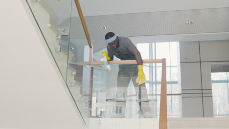 Ansicht-Von-Unten-Eines-Reinigungsmannes-Mit-Handschuhen,-Der-Treppengeländer-Und-Kristalle-In-Einem-Bürogebäude-Reinigt