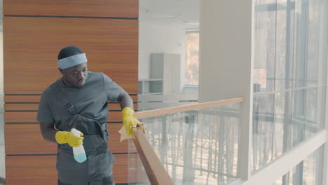 Cleaning-Man-Wearing-Gloves-Cleaning-Stair-Railing-Inside-An-Office-Building-1