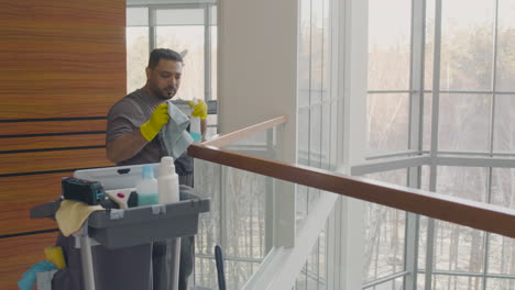Arabic-Cleaning-Man-Holding-Rag-And-Cleaning-Product-While-Dancing-Near-A-Cleaning-Cart-Inside-An-Office-Building