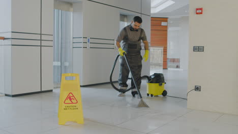 Arabic-Cleaning-Man-Cleaning-With-Pressure-Water-Machine-Inside-An-Office-Building-Behind-A-Wet-Floor-Warning-Sign