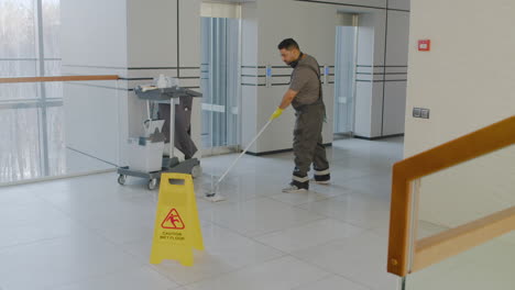 Distant-View-Of-Arabic-Cleaning-Man-Cleaning-With-Mope-Behind-A-Wet-Floor-Warning-Sign