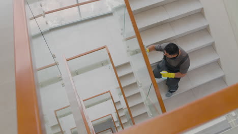 Top-View-Of-Arabic-Cleaning-Man-Wearing-Gloves-Cleaning-Stair-Railing-And-Crystals-Inside-An-Office-Building-1