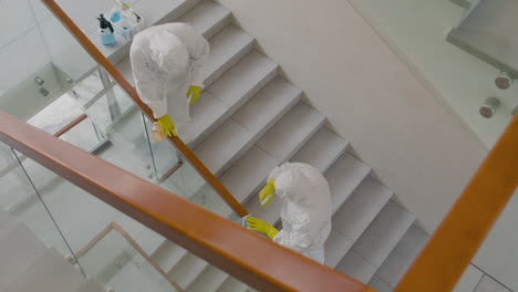 Top-View-Of-Two-Cleaning-Men-Wearing-Personal-Protective-Equipment-Cleaning-Stair-Railings-Inside-An-Office-Building-2