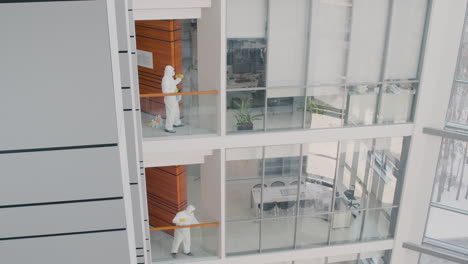 Distant-View-Of-Two-Cleaning-Men-Wearing-Personal-Protective-Equipment-Cleaning-Stair-Railings-Inside-An-Office-Building
