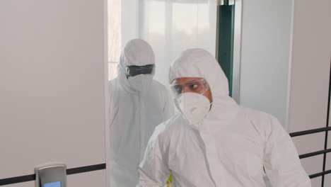Two-Cleaning-Men-Wearing-Personal-Protective-Equipment-Getting-Out-Of-Glass-Elevator-Inside-An-Office-Building