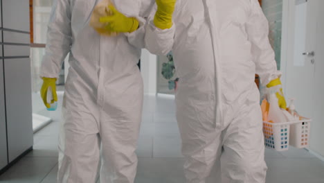 Two-Unrecognizable-Cleaning-Men-Wearing-Personal-Protective-Equipment-While-Walking-Inside-An-Office-Building-Holding-Cleaning-Products-And-Rags