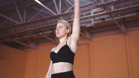 Smiling-Blonde-Sportswoman-Warming-Up-And-Stretching-Her-Body-In-An-Indoor-Sport-Facility