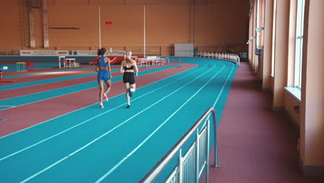 Rückansicht-Von-Zwei-Multiethnischen-Sportlerinnen,-Die-Zusammen-Auf-Einer-Indoor-Strecke-Laufen