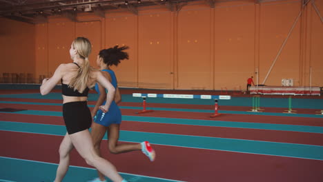 Two-Multiethnic-Female-Athletes-Running-Together-On-An-Indoor-Track-2