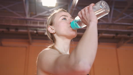 Blonde-Female-Athlete-Drinking-Water-From-Bottle-In-An-Indoor-Sport-Facility-1