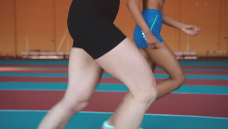 Nahaufnahme-Der-Beine-Zweier-Multiethnischer-Sportlerinnen,-Die-Zusammen-Auf-Einer-Indoor-Strecke-Laufen